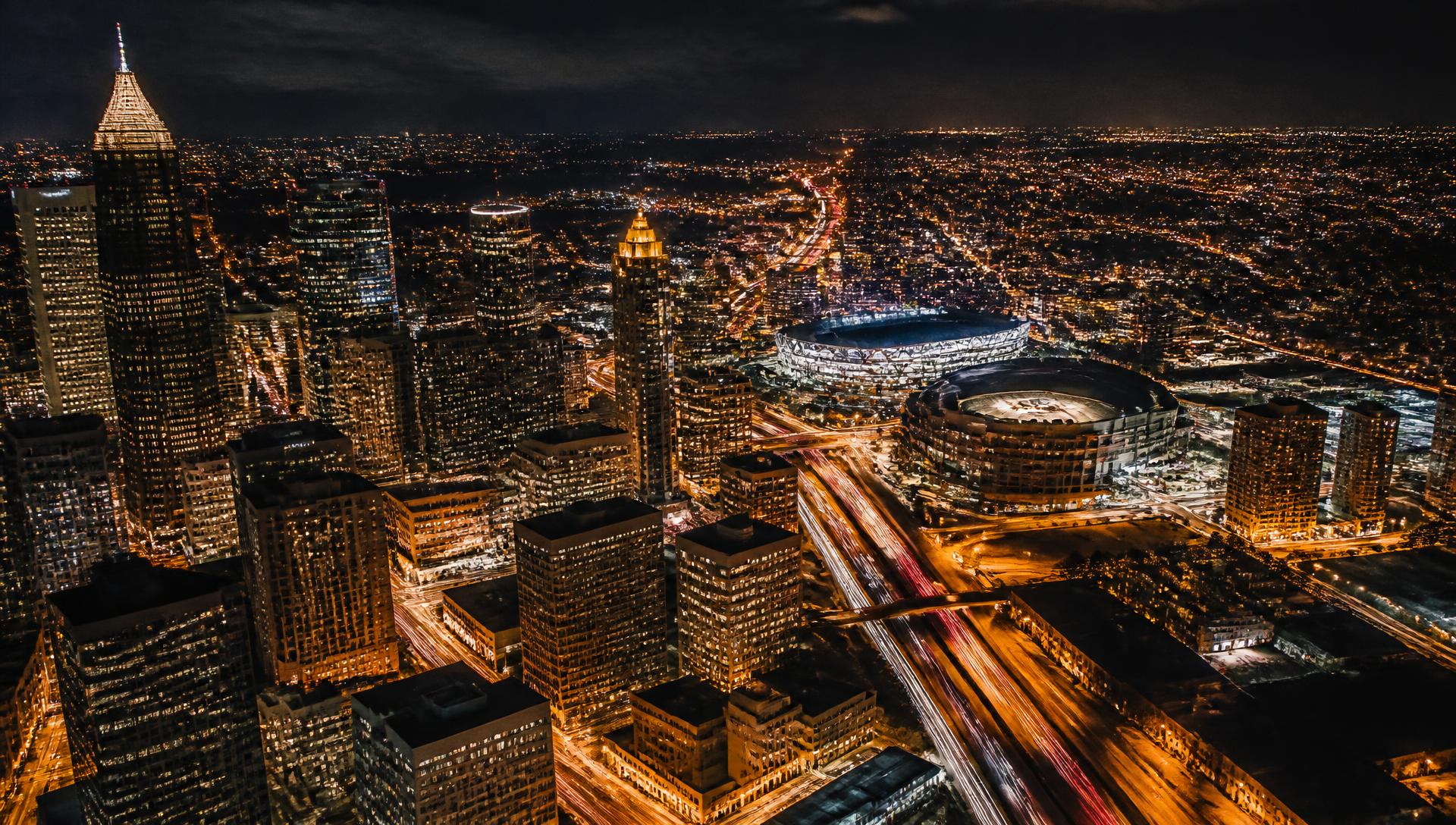 Aerial view of a city at night with lit stadiums and traffic light trails